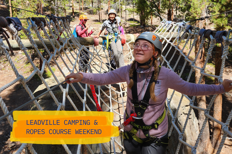 The image shows a group of people on a ropes course. A woman in the foreground is smiling and looking up, wearing a helmet and harness. Behind her, two other people are navigating the ropes course. The course appears to be set in a forest, with trees visible in the background. A banner at the bottom reads "Leadville Camping & Ropes Course Weekend."